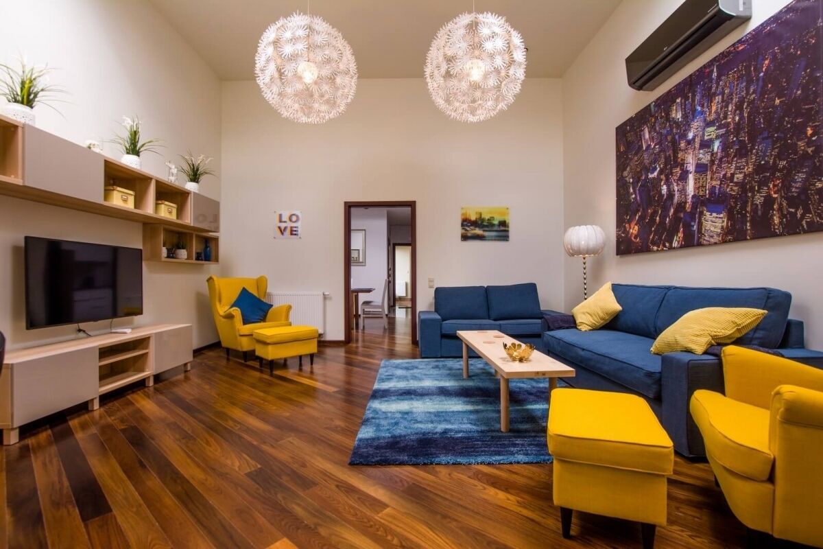 A modern living room with a TV, yellow armchairs, a blue sofa, and a cityscape painting.