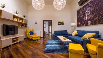 A modern living room with a TV, yellow armchairs, a blue sofa, and a cityscape painting.