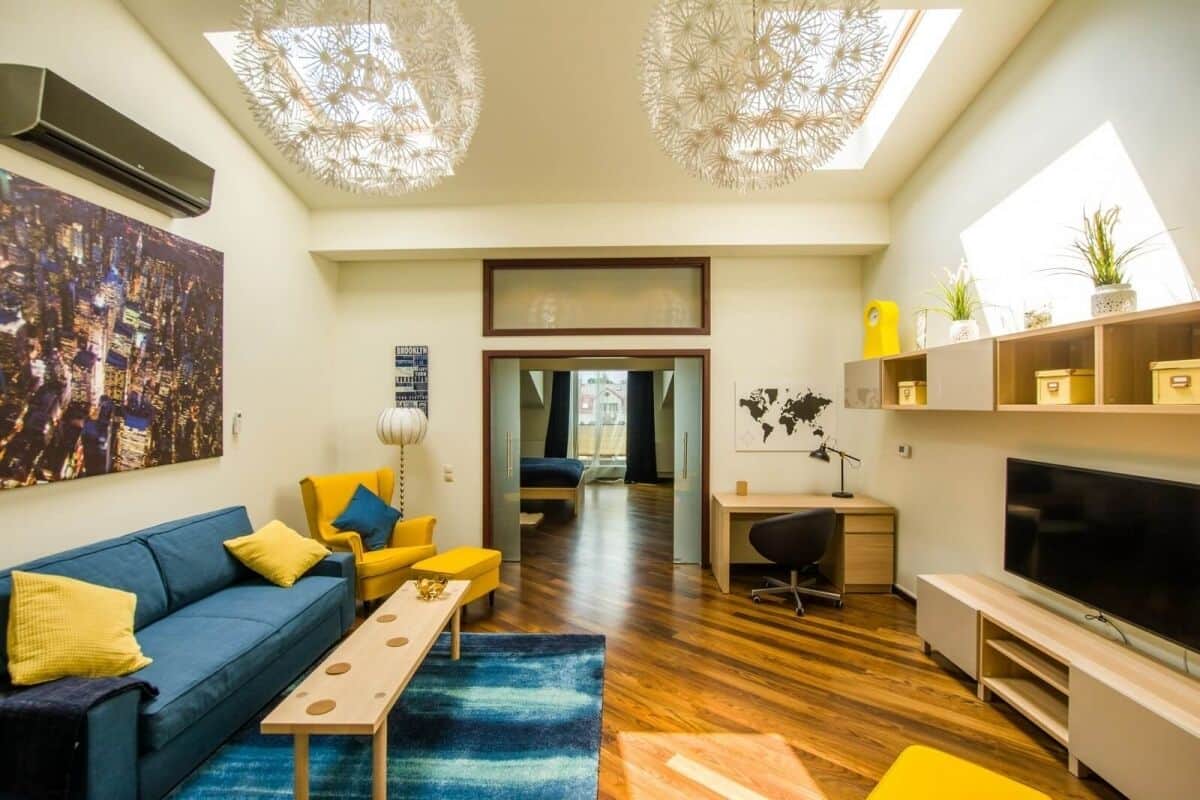 Una sala de estar moderna con un sofá azul, sillones amarillos, una mesa de centro y un televisor.