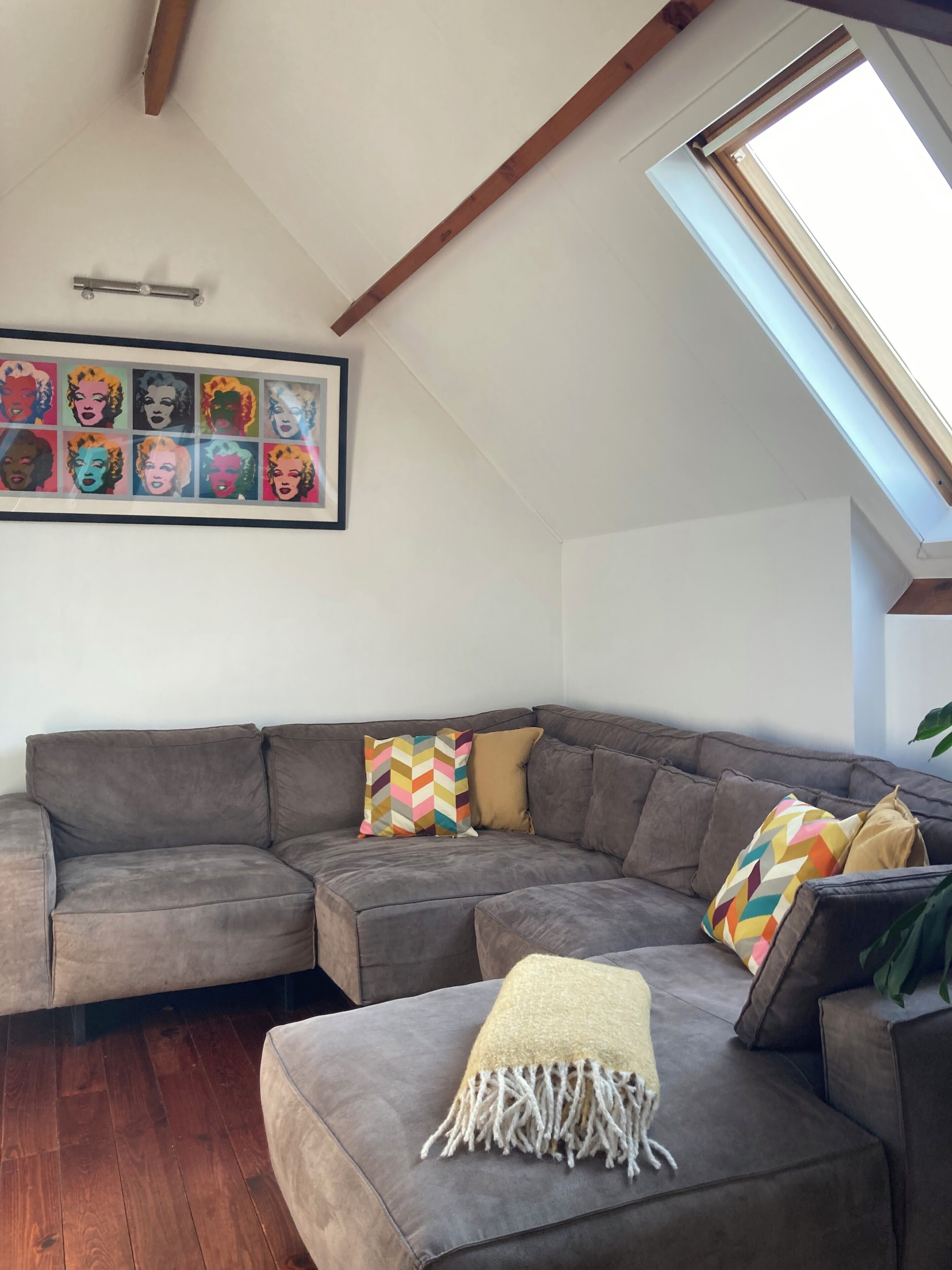 A modern living room with a gray sectional sofa, colorful geometric pillows, a throw blanket, and a framed pop art print on the wall.