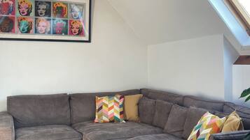 A modern living room with a gray sectional sofa, colorful geometric pillows, a throw blanket, and a framed pop art print on the wall.