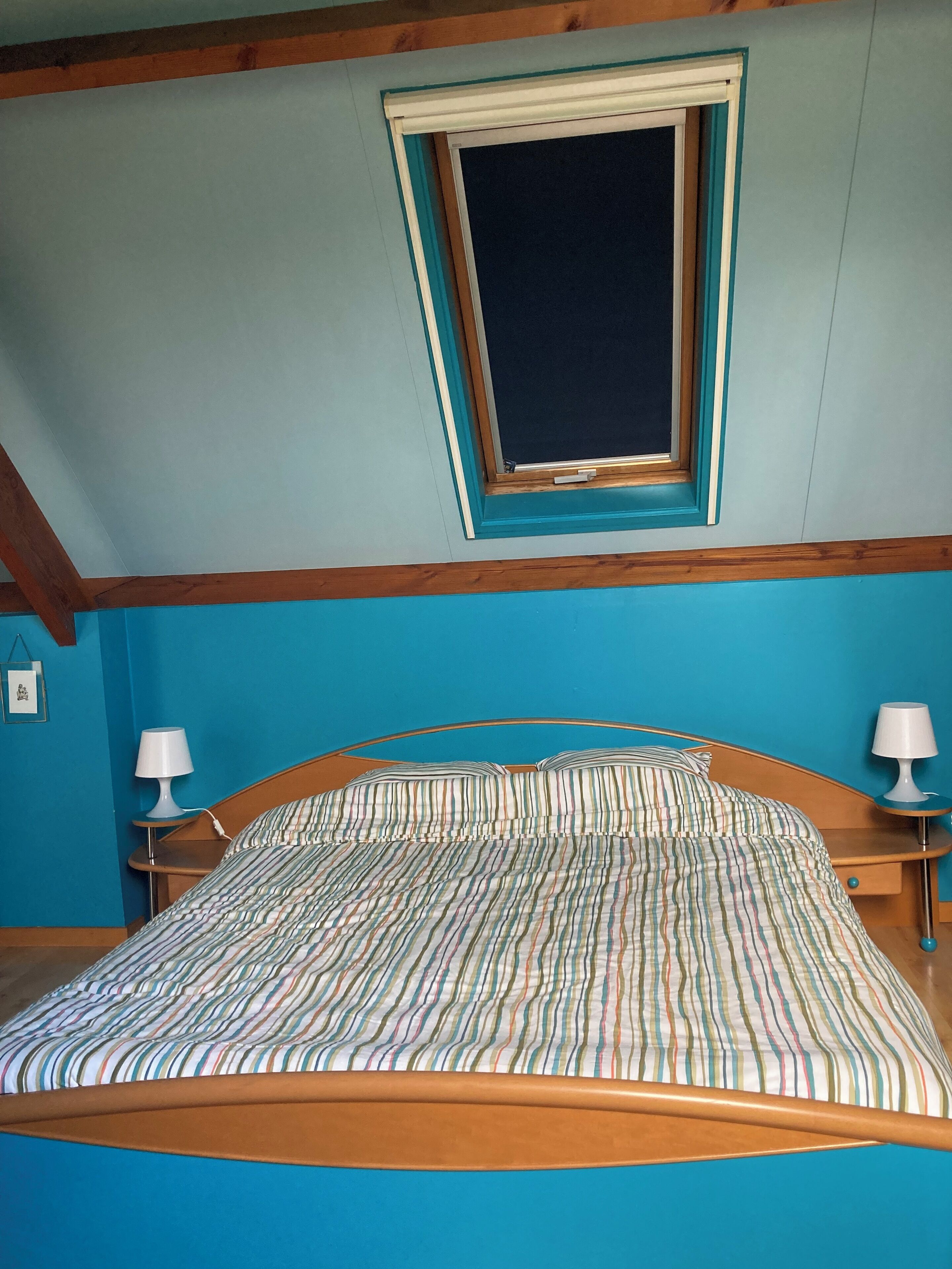 Una camera da letto con un letto, due comodini con lampade, una finestra e un soffitto spiovente.