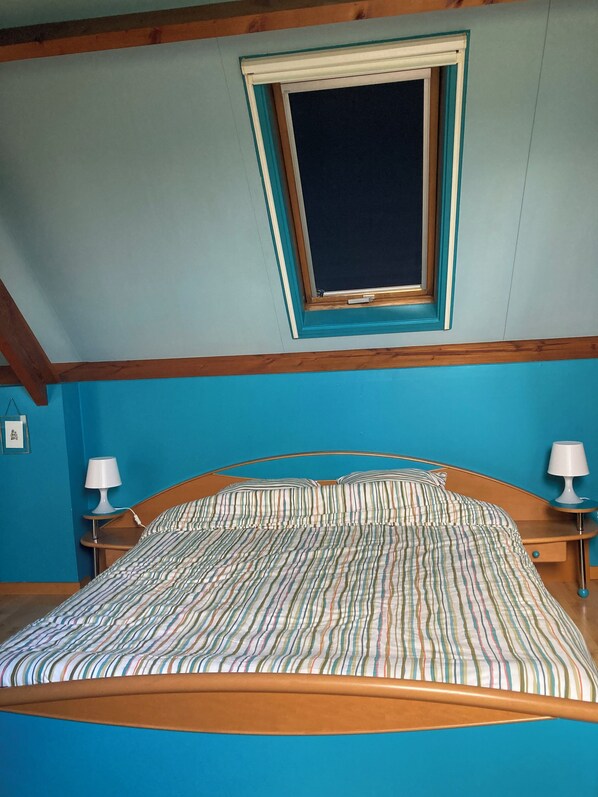 Un dormitorio con cama, dos mesitas de noche con lámparas, una ventana y techo inclinado.