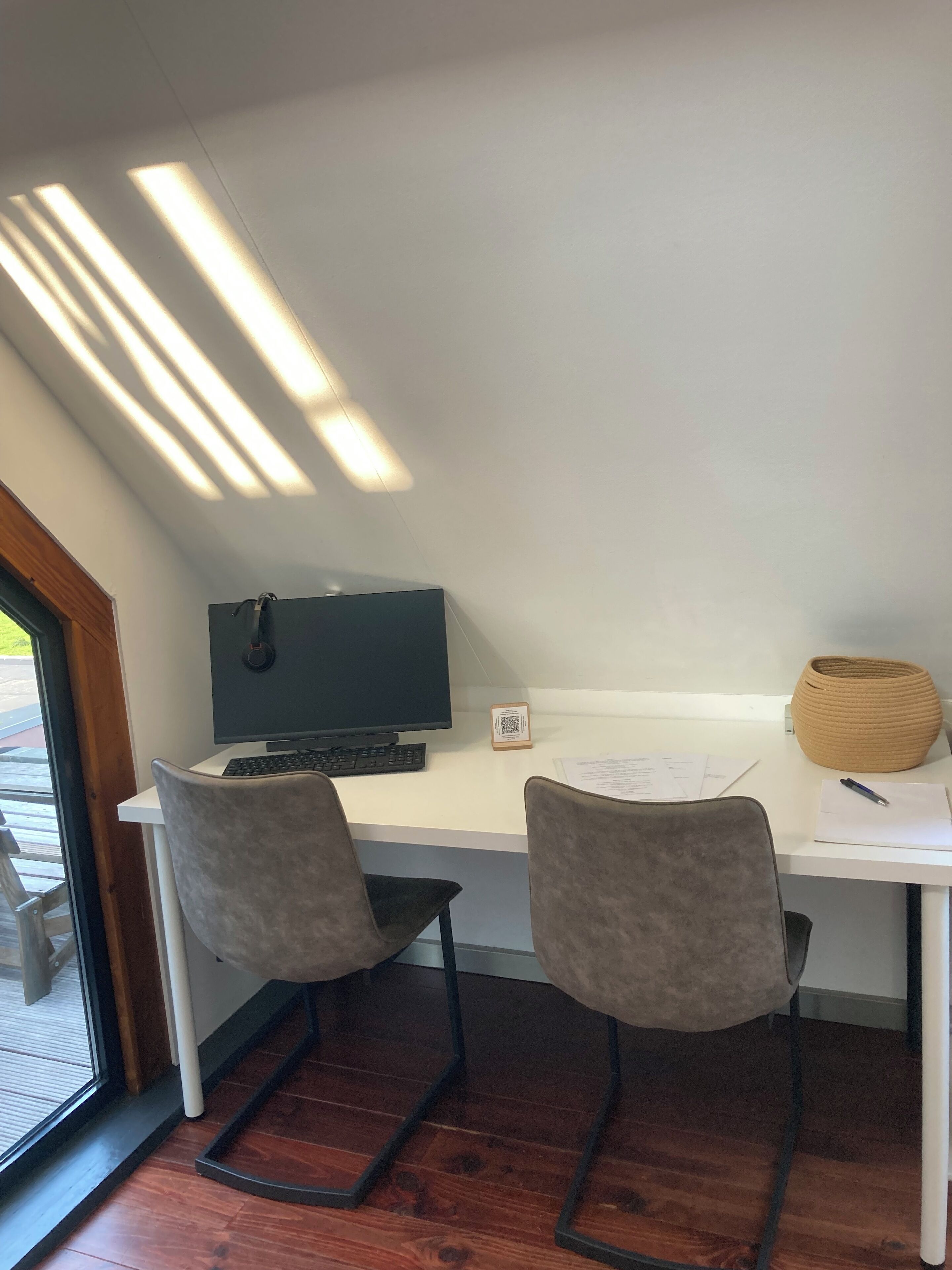 Een moderne kantoorruimte met een bureau, twee stoelen, een computer en een raam met jaloezieën.