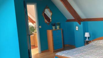 Une chambre avec un plafond en pente, un lit, une commode et un miroir.