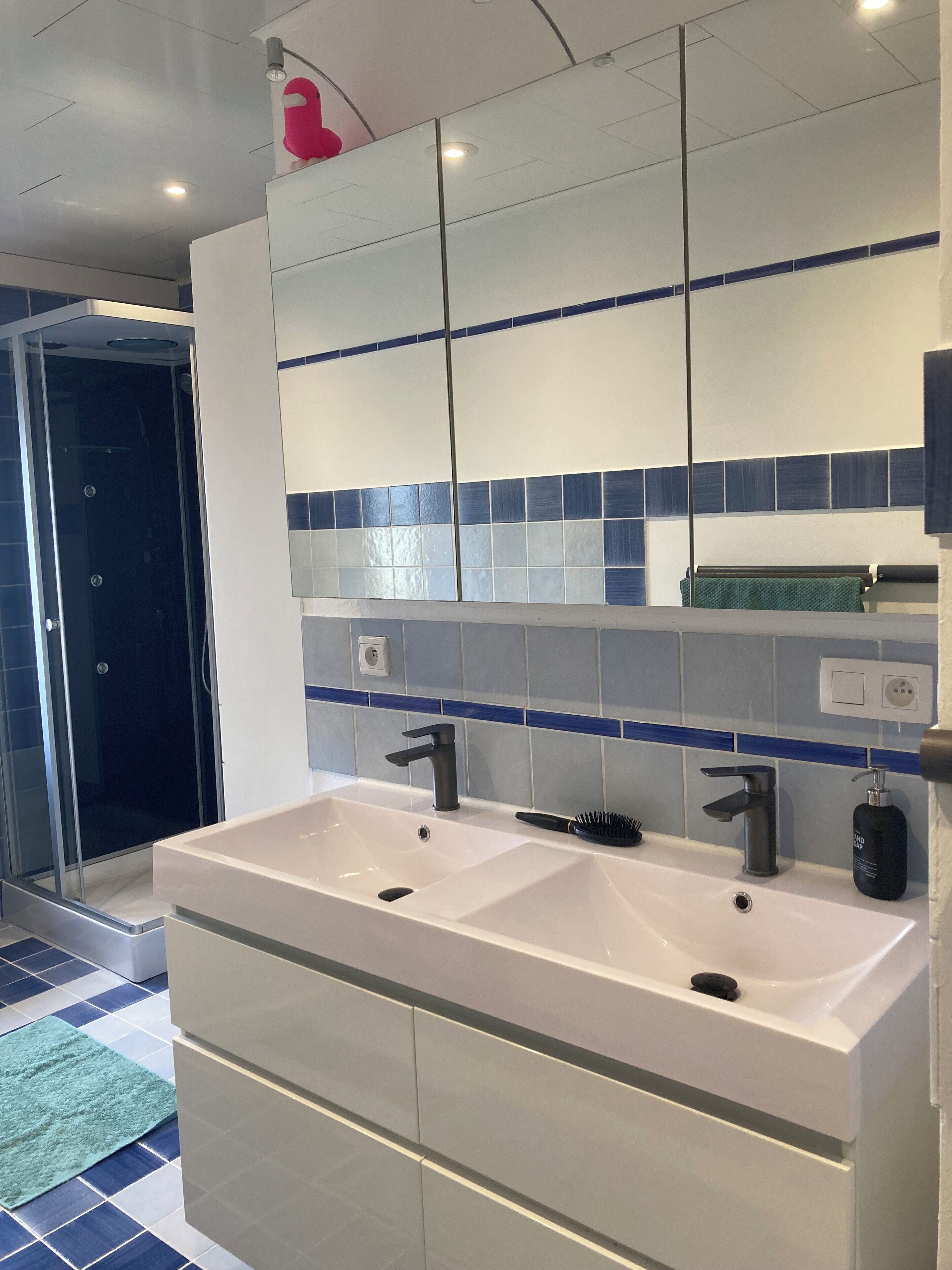 Een moderne badkamer met een grote spiegel, twee wastafels en een douche.