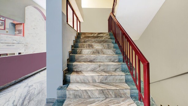 A marble staircase with a red railing leading to a landing. - Super Hotel O East Nada (Chavakkad)