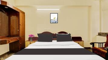 A hotel room with a bed, a wooden wardrobe, a nightstand with a vase of flowers, and a framed picture on the wall.