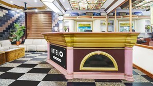 Un espace d’accueil d’hôtel comprenant un comptoir d’enregistrement, un bureau de réception, une horloge et un panneau indiquant « Réception ».