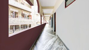 Un couloir doté d’un sol en marbre, de fenêtres à encadrement rouge et d’un mur en briques sur un de ses côtés.