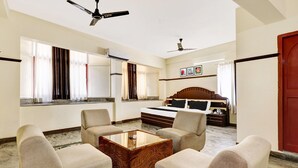 Une chambre d’hôtel comprenant un canapé, une table basse en bois, un lit avec une tête de lit et deux ventilateurs de plafond.