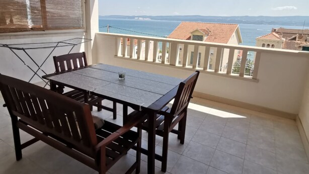 Un balcón con una mesa y sillas, con vistas a la costa, edificios y el mar.