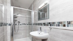 A modern bathroom with a glass-enclosed shower, a white pedestal sink, and a mirror above the sink. - Annan Hotel (Llandudno)