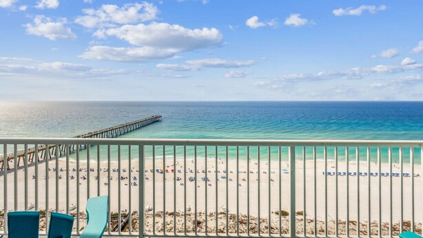 A beach view with a pier extending into the ocean, a sandy beach with people, and a clear sky.