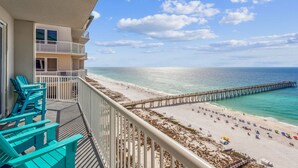 A balcony with turquoise chairs overlooking a beach with a pier.