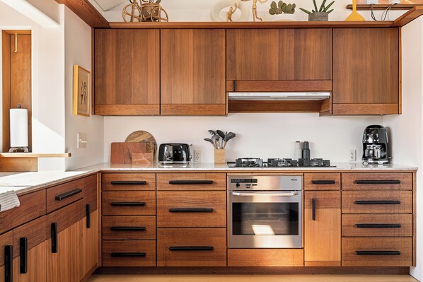 A modern kitchen with wooden cabinets, a built-in oven, and a coffee maker.