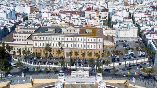 Vue aérienne d’une ville côtière, avec un imposant bâtiment blanc doté d’un dôme et une vaste place publique en premier plan.