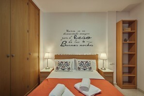 A neatly made bed with two decorative pillows, a wooden wardrobe, and a shelf unit.