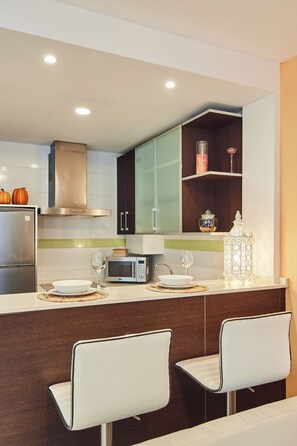 A modern kitchen with a refrigerator, microwave, and a dining area with two chairs.