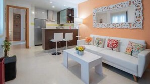 Un salon moderne avec un canapé blanc, une table basse ornée de fleurs et une cuisine en arrière-plan.