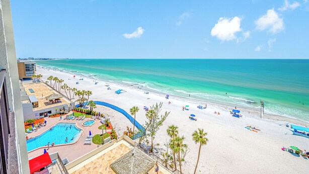 A beach resort with a swimming pool, palm trees, and a view of the ocean.
