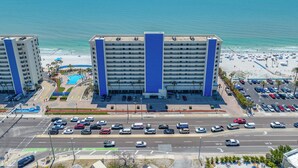 A hotel with multiple floors, a parking lot, and a beach view.