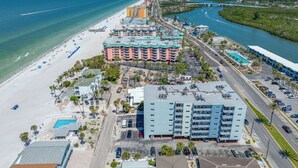Vue aérienne d’un hôtel situé sur la côte, avec une plage, une piscine et un port de plaisance.