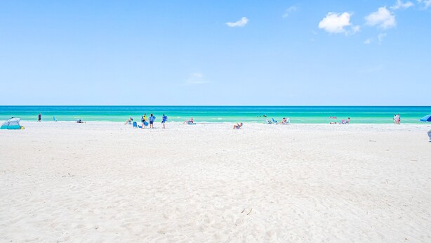 Une vaste plage de sable fin bordée d’une eau turquoise et limpide, avec quelques personnes et des chaises de plage.