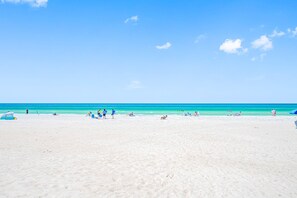 A wide sandy beach with clear turquoise water, a few people, and beach chairs. - San Remo 501- Beautiful Beachfront Escape! (Redington Beach)