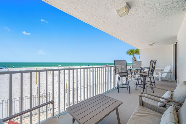 A balcony with a view of the beach, a table, chairs, and a potted plant.