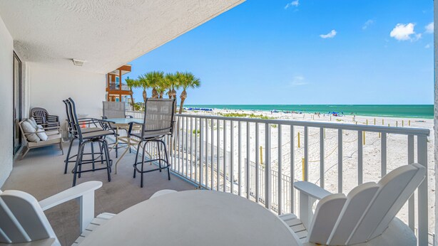 A balcony with a table and chairs, a view of the beach, and a palm tree.