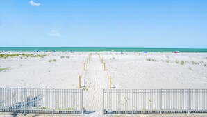 A beach with a sandy path leading to the water, a white fence, and a clear blue sky.