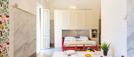 A compact room with a bed, a dining table with chairs, a small kitchen area, and a bathroom with a shower.