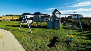 Un parque infantil con diversas estructuras de juego, un cielo despejado y una zona cubierta de césped.
