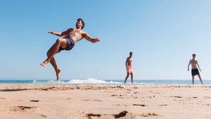 Escena de playa con una persona saltando y un disco volador en el aire, y otras dos personas caminando al fondo.