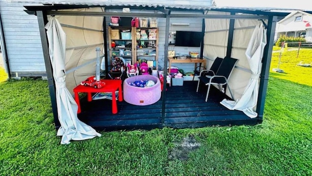 Un espacio al aire libre techado con una mesa, sillas, un coche de juguete rojo y un área de juegos con pelotas moradas.