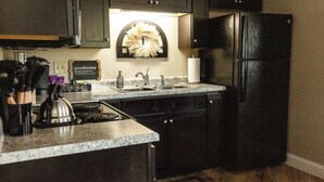 A kitchen with dark cabinets, a stainless steel kettle, a sink, and a black refrigerator. - Cambrian & Co. Downtown Loft Stylish, Sophisticated, Charm (Taylors Falls)