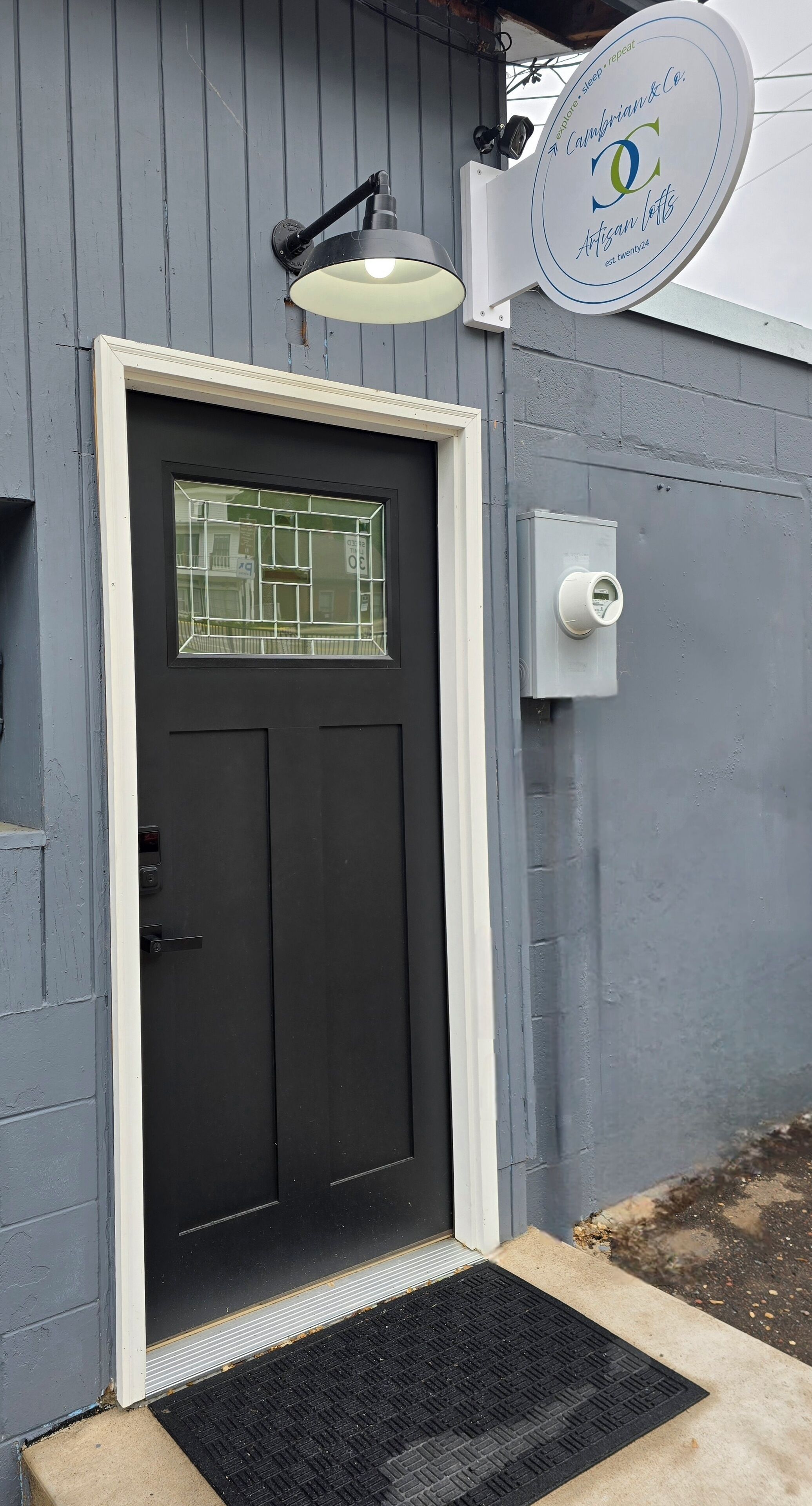 A black door with a glass panel, a white mailbox, and a street lamp above.