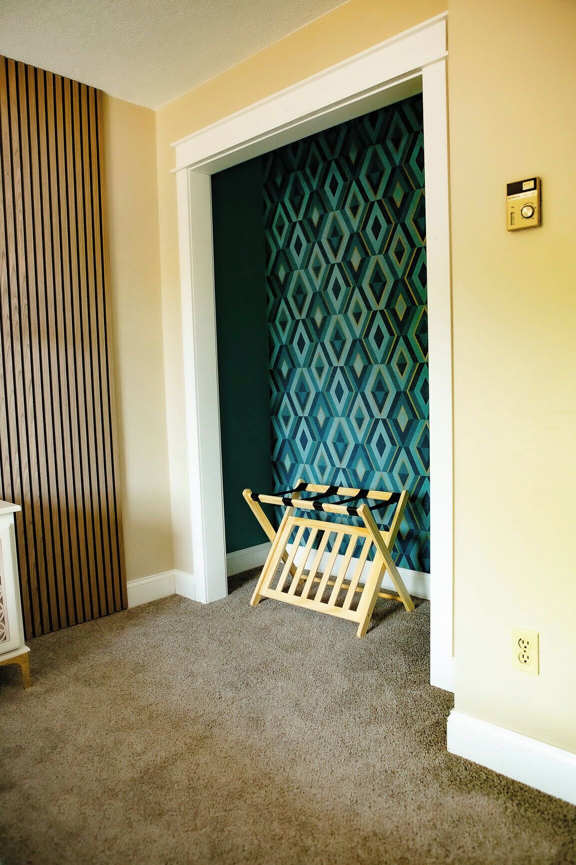 Una habitación con papel tapiz estampado, un banco de madera y suelo alfombrado.