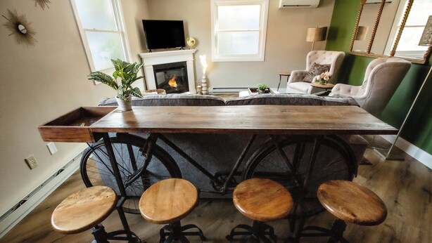 A kitchen with a wooden island, bar stools, a fireplace, and a television. - Cambrian & Co. Downtown Loft Stylish, Sophisticated, Charm (Taylors Falls)