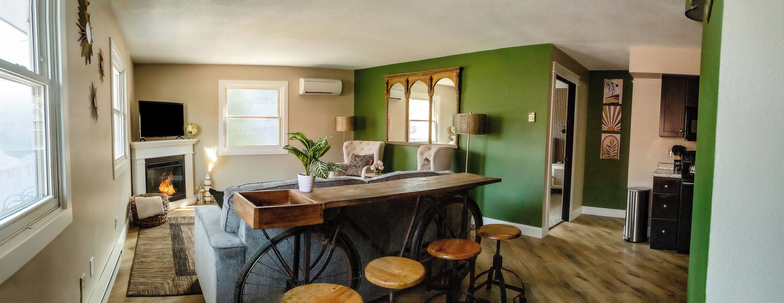 Un salon chaleureux avec une cheminée, un mur d’accent vert et un coin bar avec des tabourets.