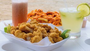 A beachside table with a plate of fried chicken, a drink with a lime garnish, and a drink with a straw. - MAR E PRAIA HOTEL (Ubatuba)