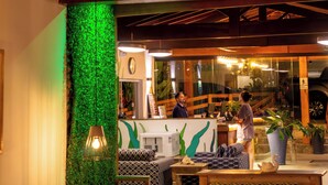 A reception area with a green wall, wooden furniture, and a counter. - MAR E PRAIA HOTEL (Ubatuba)