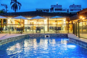 Piscina com espreguiçadeiras e guarda-sóis, cercada por edifícios com varandas e telhado em azulejos.