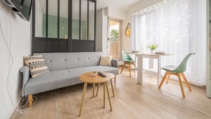 Ein modernes Wohnzimmer mit einem grauen Sofa, einem runden Holztisch und einem Essbereich mit einem weißen Tisch und grünen Stühlen.