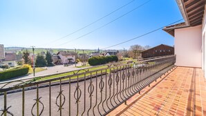 A balcony with a metal railing overlooking a street with houses and a clear sky.