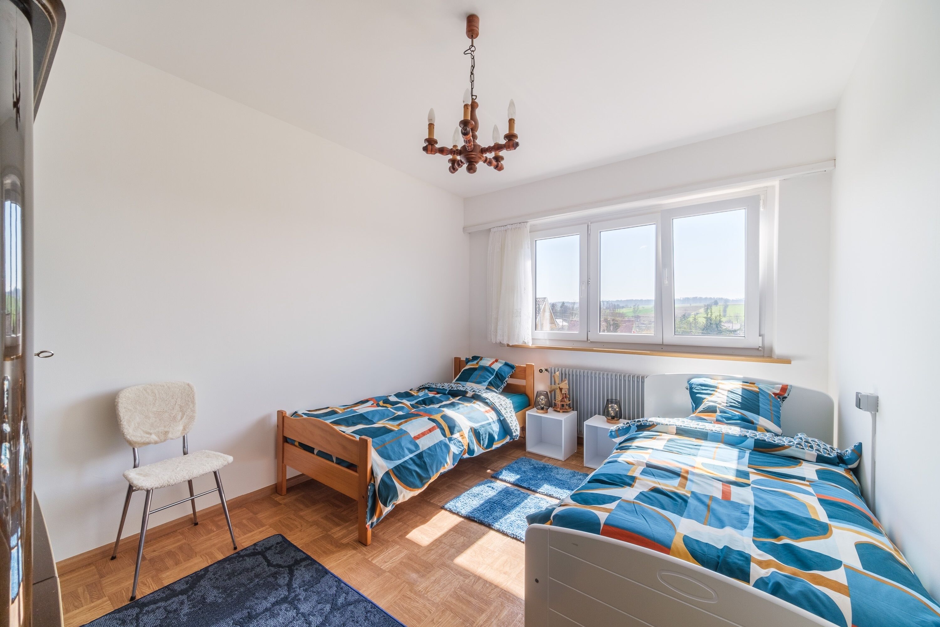 Une chambre avec deux lits, une chaise, un radiateur et une fenêtre donnant sur un beau paysage.