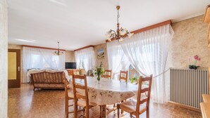A dining area with a round table, wooden chairs, a chandelier, and a radiator.