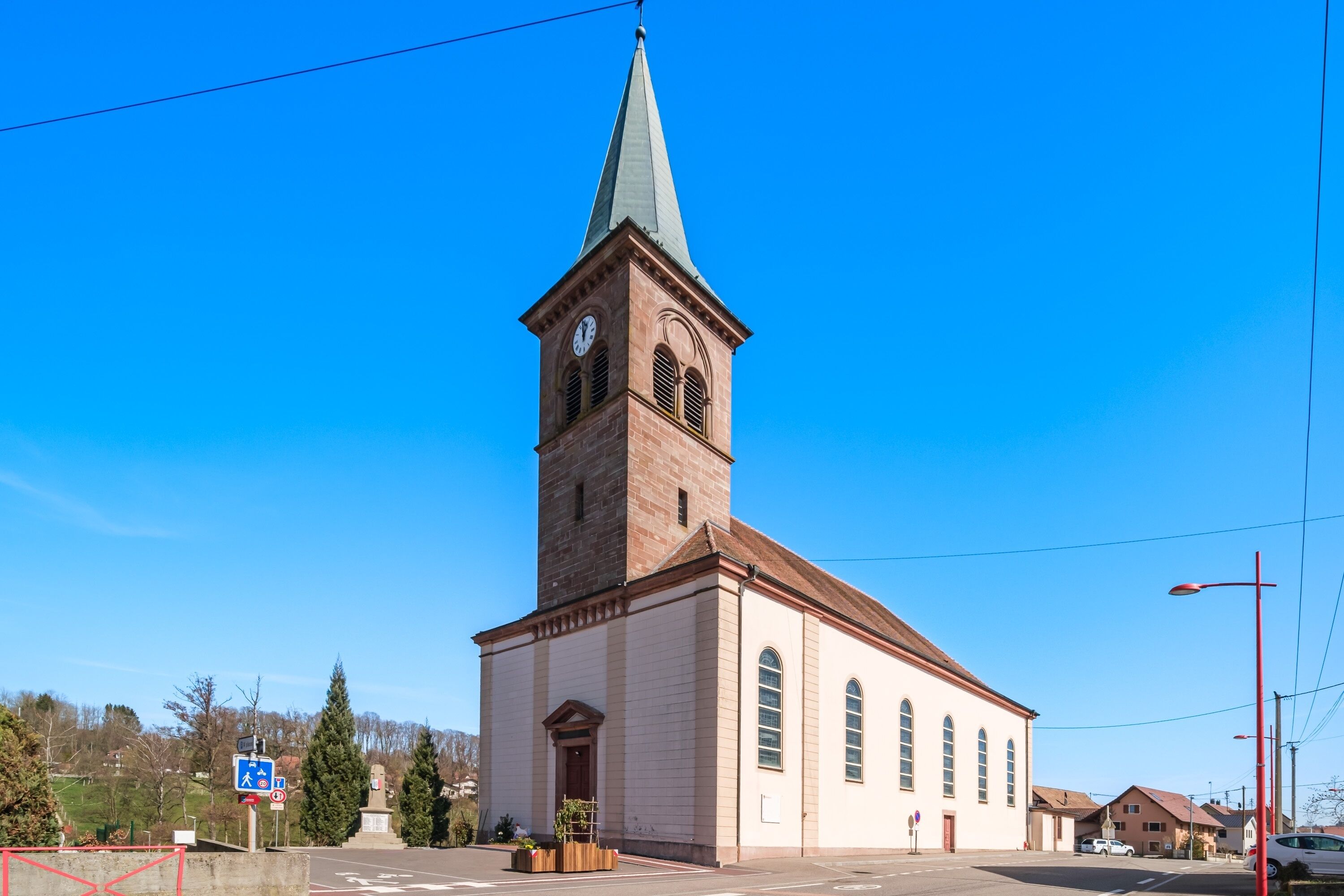 Eine Kirche mit hohem Turm und einer Uhr, einem klaren blauen Himmel und einer Straße im Vordergrund.