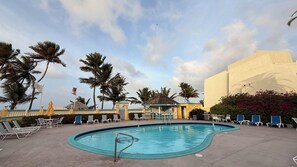 A swimming pool with lounge chairs, palm trees, and a building in the background. - Welcome to DEJA BLUE a Beach front condo in a gated complex!! (St Croix)